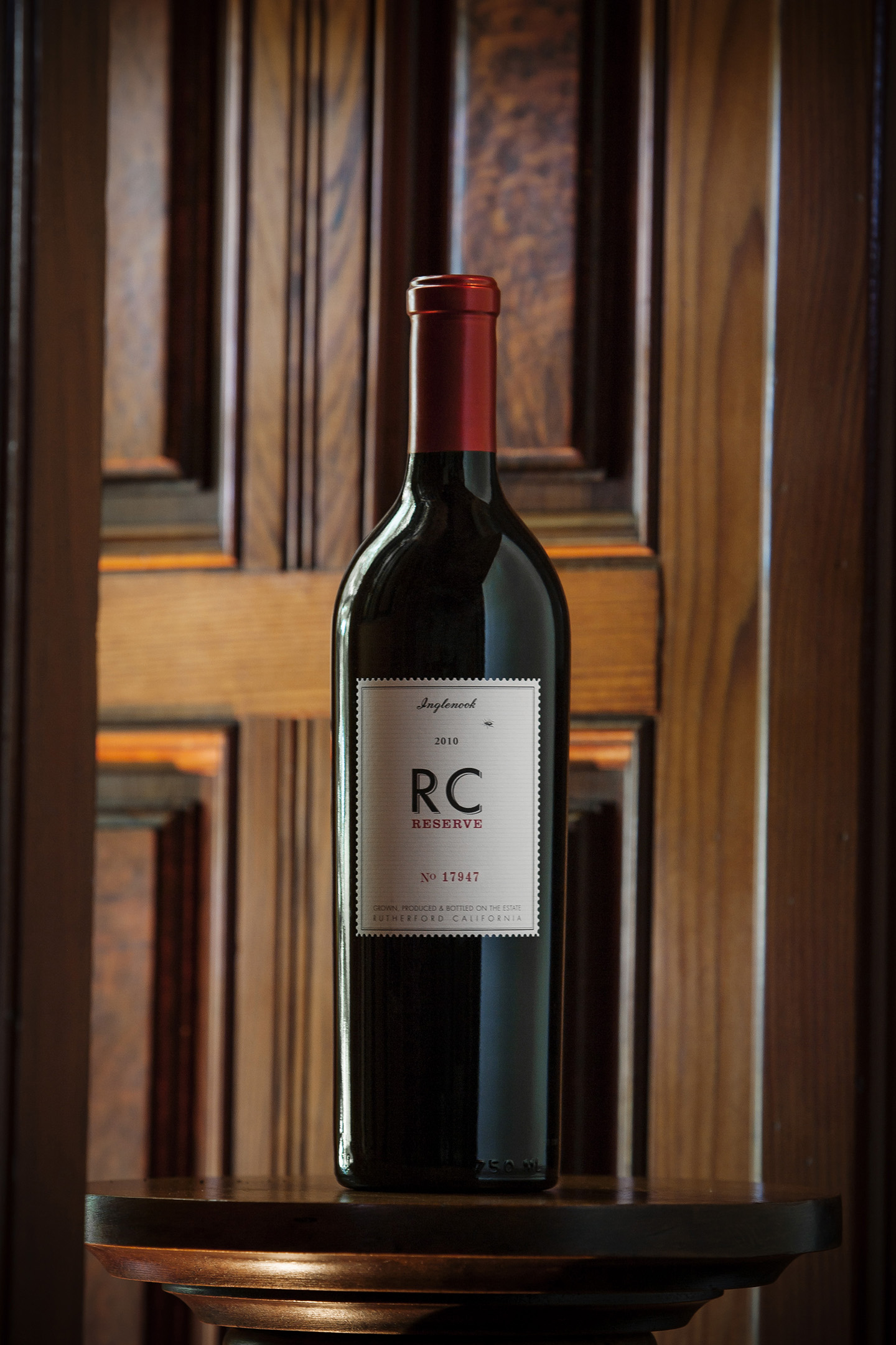 Bottle of RC Reserve Syrah wine sitting on a wooden ledge in front of dark wood paneling.