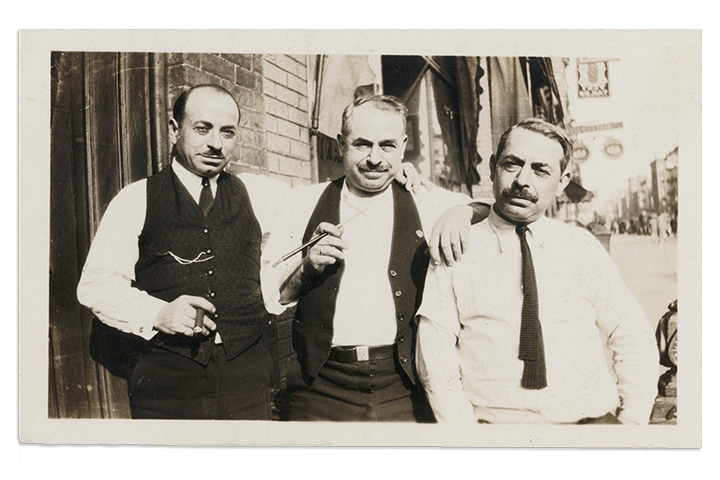 Black and white photo of three men standing on a street.